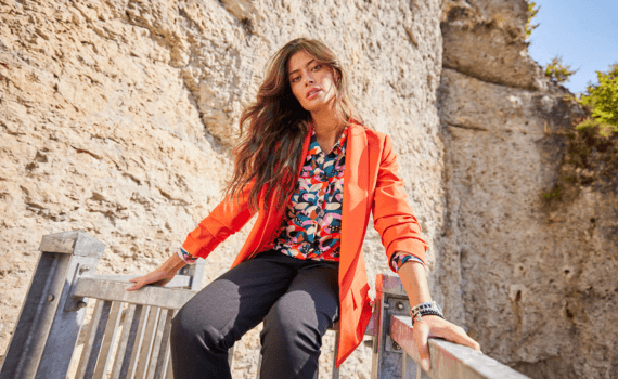 Vrouw in een oranje blazer zittend op een leuning in de bergen